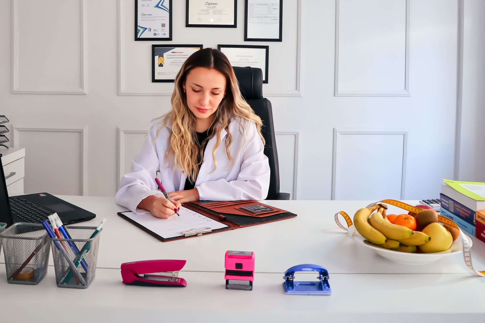 Paperasse administrative d'une professionnelle indépendante : dossier à remplir, tampon, et diplômes encadrés au mur.